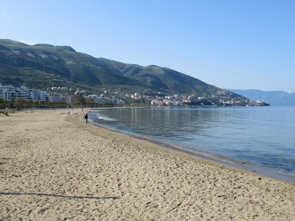 A long sandy beach in Vlore with calm waters and a view of the mountains